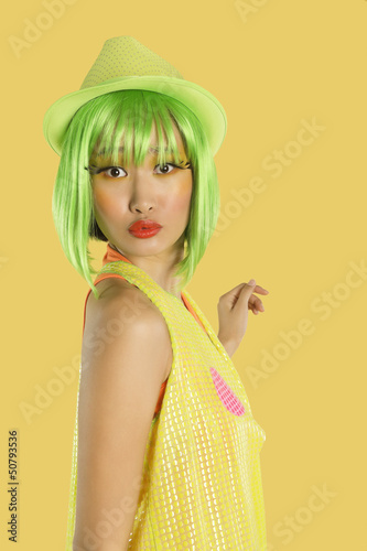 Photo: Portrait of funky young woman with green hair puckering her lips against yellow background Portrait of funky young woman with green hair puckering her lips against yellow background