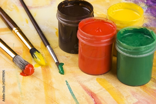 Photo: Paints and brushes againts painted multicolored background Paints and brushes againts painted multicolored background