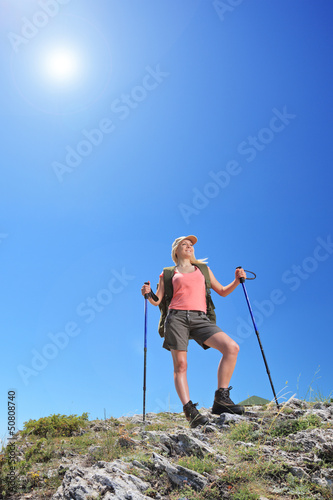 Photo: A young female with backpack and hiking poles posing at sunny da A young female with backpack and hiking poles posing at sunny da