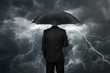 Businessman with umbrella standing in front of storm