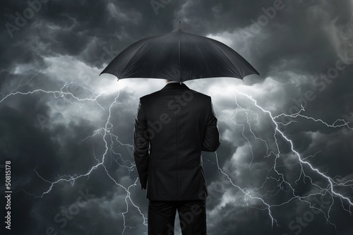 Photo: Businessman with umbrella standing in front of storm Businessman with umbrella standing in front of storm