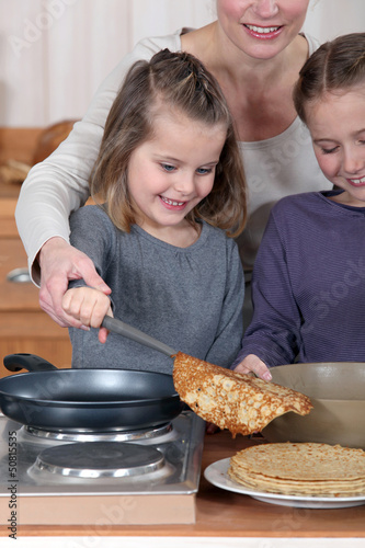 Photo: Mother making pancakes with her two daughters Mother making pancakes with her two daughters