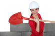 Woman stood by unfinished wall with spade