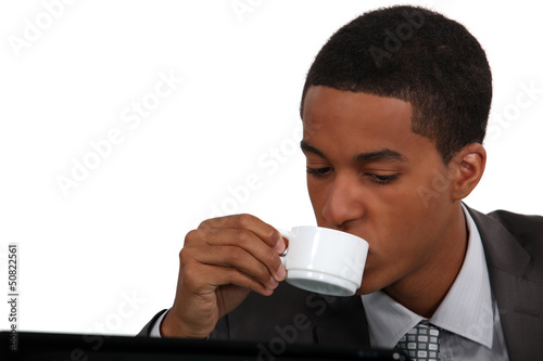 Photo: Businessman drinking coffee by laptop Businessman drinking coffee by laptop