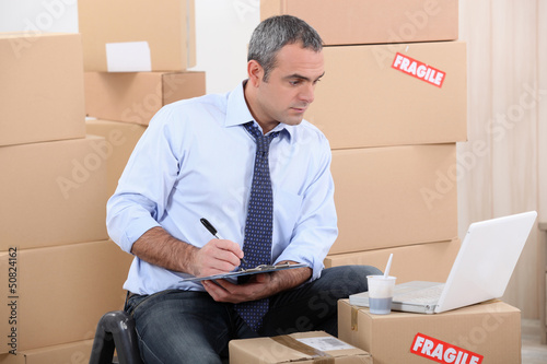 Photo: Man surrounded by cardboard boxes using a laptop Man surrounded by cardboard boxes using a laptop