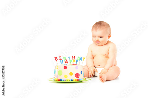 Photo: A 9 month old baby in diapers sitting next to a birthday cake A 9 month old baby in diapers sitting next to a birthday cake