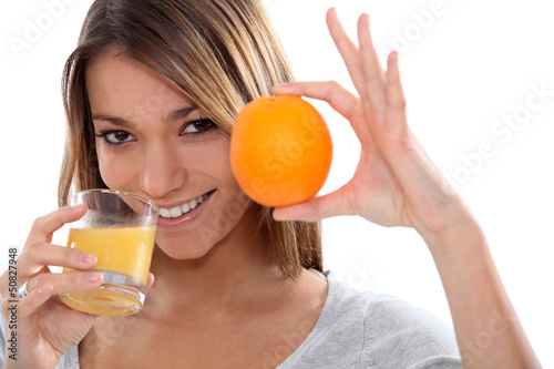 Photo: Woman holding up an orange and drinking orange juice Woman holding up an orange and drinking orange juice
