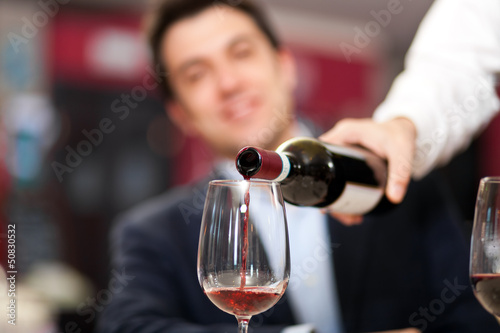 Photo: Waiter pouring red wine to a man Waiter pouring red wine to a man