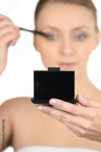 Photo: Woman applying mascara looking at a compact mirror Woman applying mascara looking at a compact mirror