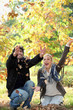 joyful couple playing with dead leaves in autumn