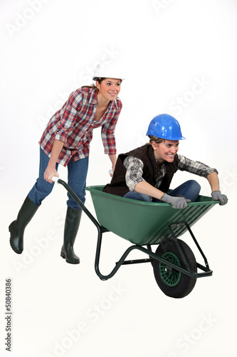 Photo: Two female construction workers racing in a wheelbarrow. Two female construction workers racing in a wheelbarrow.