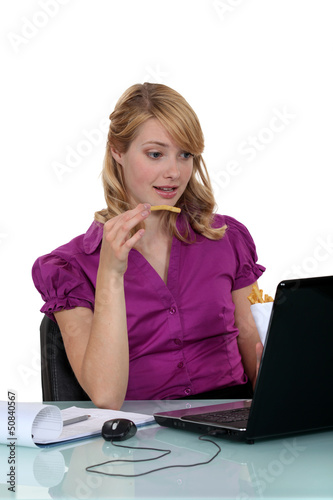 Photo: Employee eating French fries in front of her computer Employee eating French fries in front of her computer