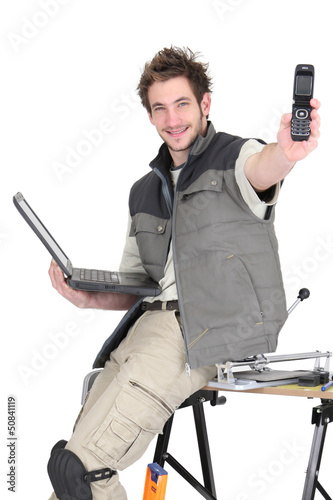 Photo: Tradesman holding a mobile phone and a laptop Tradesman holding a mobile phone and a laptop