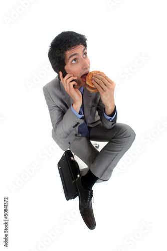 Photo: Businessman on the phone eating hamburger Businessman on the phone eating hamburger