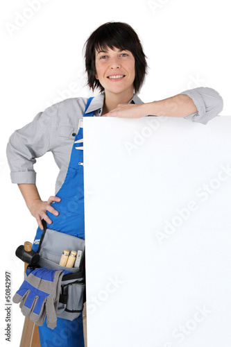 Photo: Female carpenter with a board left blank for your message Female carpenter with a board left blank for your message