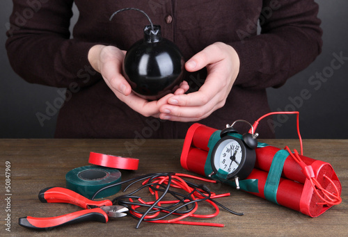 Photo: Human makes timebomb on wooden table on black background Human makes timebomb on wooden table on black background