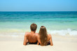 Young couple sitting together on a sand by sea and looking to a