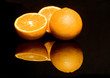 Drei Orangen spiegeln sich auf schwarzer Flaeche
