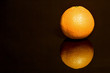 Eine Orange spiegelt sich auf schwarzer Flaeche
