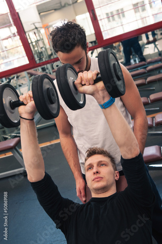 Photo: Young man and his personal trainer exercising with dumbbells Young man and his personal trainer exercising with dumbbells