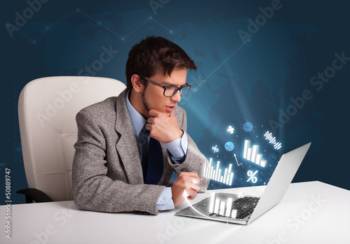 Photo: Young man sitting at desk and typing on laptop with diagrams and Young man sitting at desk and typing on laptop with diagrams and