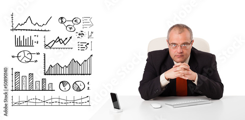 Photo: Businessman sitting at desk with diagrams and graphs Businessman sitting at desk with diagrams and graphs
