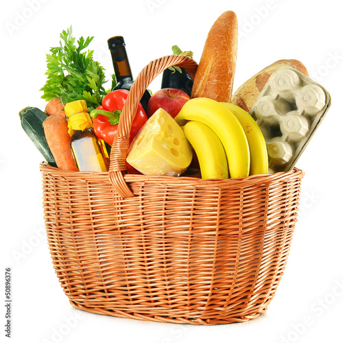 Photo: Wicker basket with variety of grocery products isolated on white Wicker basket with variety of grocery products isolated on white