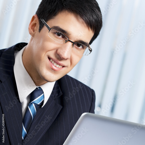 Photo: Smiling businessman working with laptop at office Smiling businessman working with laptop at office