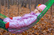 Thoughtful girl swinging in hammock in autumn forest