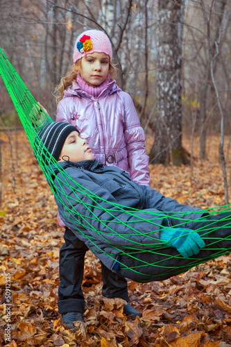 Photo: A boy with his sister relaxing in hammock in autumn forest A boy with his sister relaxing in hammock in autumn forest