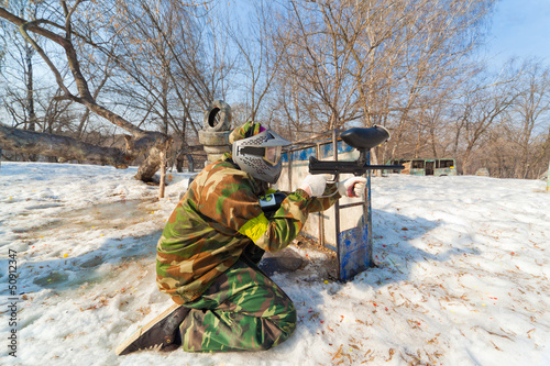 Photo: player in a paintball aims for shelter in game on sunny day player in a paintball aims for shelter in game on sunny day