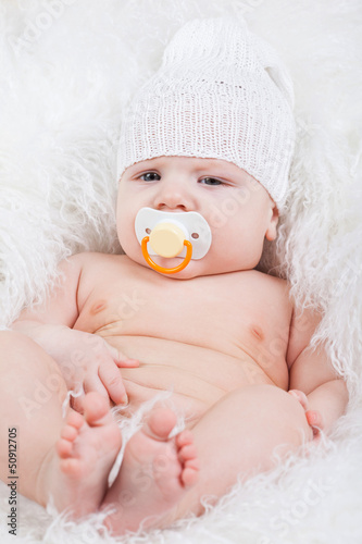 Photo: Portrait of a baby with a pacifier in white hat Portrait of a baby with a pacifier in white hat