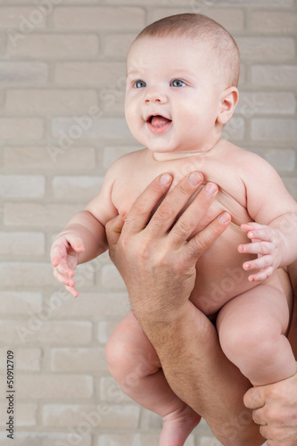 Photo: Smiling baby in arms of father. Baby looks into the distance. Smiling baby in arms of father. Baby looks into the distance.