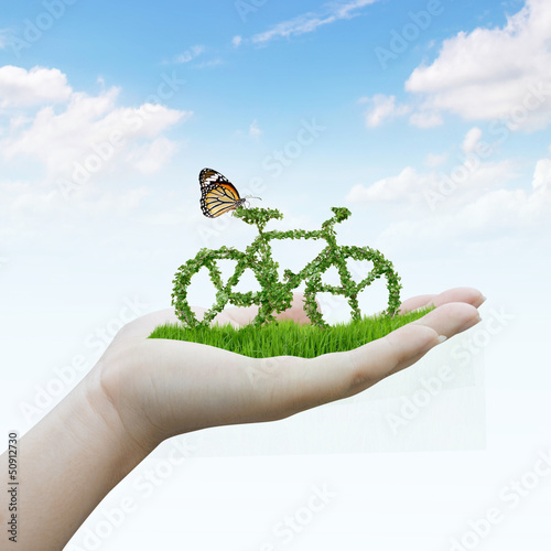 Photo: hand holding bicycle made out of green leaves hand holding bicycle made out of green leaves