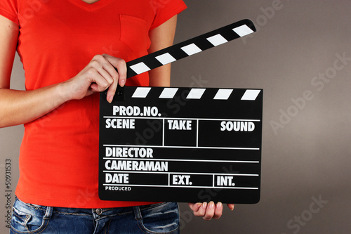 Photo: Movie production clapper board in hands on grey background Movie production clapper board in hands on grey background