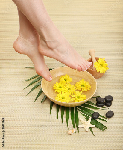 Photo: Female feet in spa bowl with water, on bamboo mat Female feet in spa bowl with water, on bamboo mat