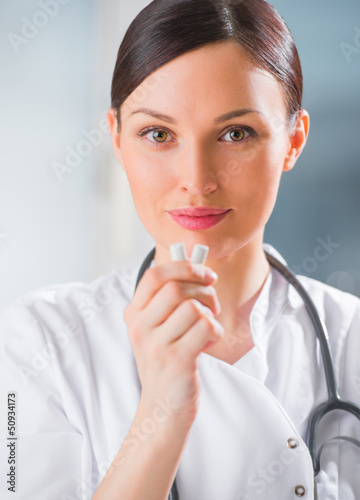 Photo: Young female dentist doctor holding chewing gum and smiling. Den Young female dentist doctor holding chewing gum and smiling. Den