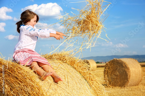 Photo: small rural girl on harvest field with straw bales small rural girl on harvest field with straw bales