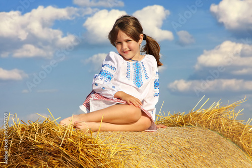 Photo: small rural girl on the straw after harvest field with straw bal small rural girl on the straw after harvest field with straw bal