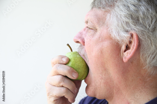 Photo: senior man eats a fresh pear senior man eats a fresh pear