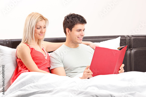 Photo: Young couple lying on a bed and reading a book Young couple lying on a bed and reading a book