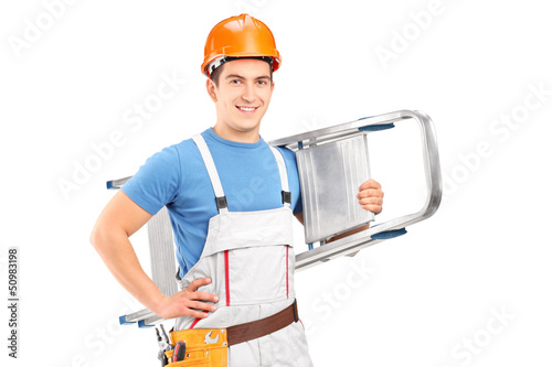 Photo: A manual worker with a helmet carrying a ladder A manual worker with a helmet carrying a ladder