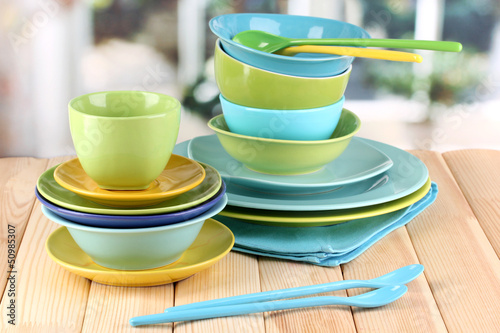 Photo: Colorful tableware on wooden table on window background Colorful tableware on wooden table on window background