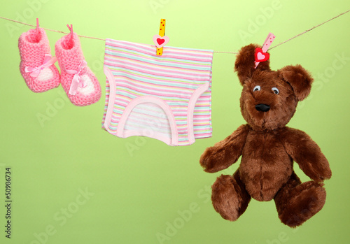 Photo: Baby clothes hanging on clothesline, on color background Baby clothes hanging on clothesline, on color background