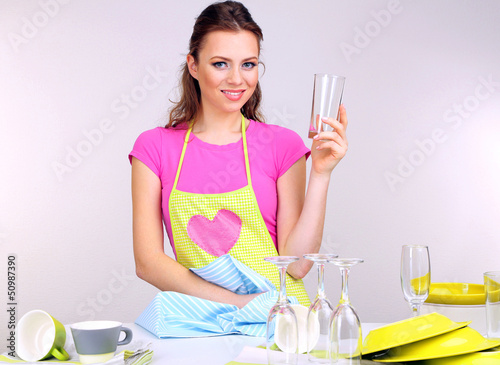 Photo: Beautiful young woman wipes clean utensils in kitchen Beautiful young woman wipes clean utensils in kitchen