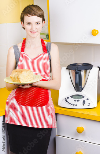 Photo: Cute baking woman holding fresh bread in kitchen Cute baking woman holding fresh bread in kitchen