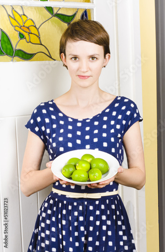 Photo: Beautiful girl holding bowl of green limes Beautiful girl holding bowl of green limes