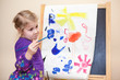 Photo: Cute Caucasian girl standing with painting brush near easel Cute Caucasian girl standing with painting brush near easel