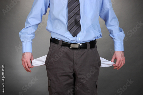 Photo: Business man showing his empty pockets, on grey background Business man showing his empty pockets, on grey background