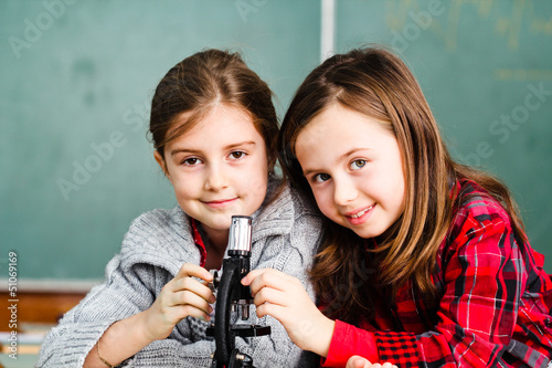 Photo: Two schoolgirls have a practice with microscope Two schoolgirls have a practice with microscope